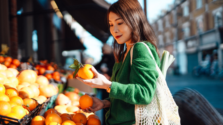 Woman looking at an orange while shopping at a farmers market