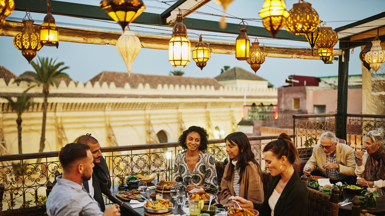 Crowded restaurant balcony with ornate lamps and desert buildings in background