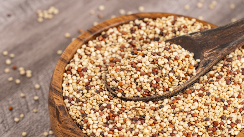 A close up of a wooden bowl of quinoa with a spoon in it.