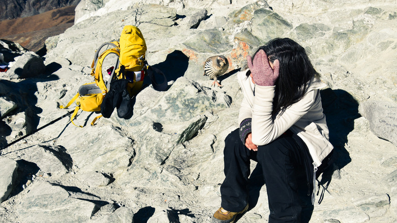 A young woman sitting on a rocky mountaintop, wearing gloves with her head in her hands