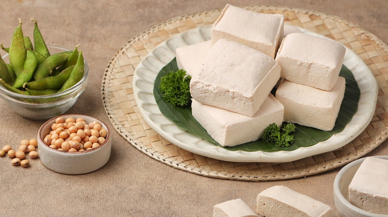 White tofu blocks sitting on a dish with peas and beans in containers sitting next to it.