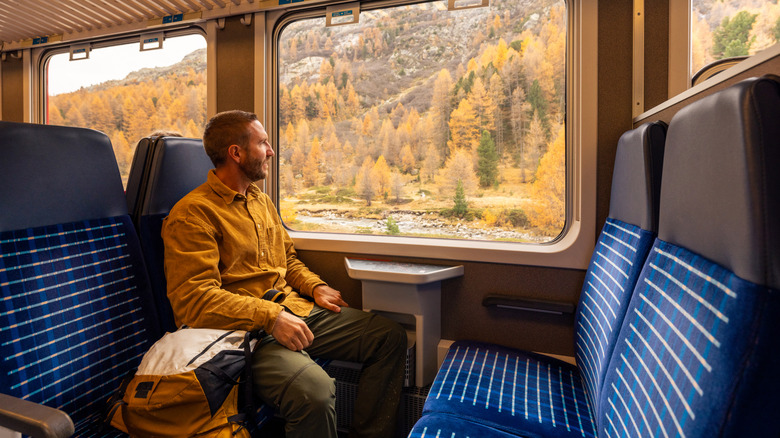 Man in yellow shirt on train looks at the views through the window.