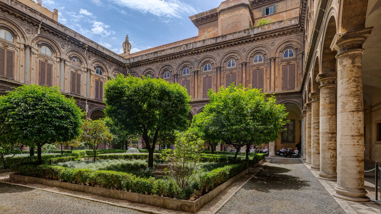 A plaza outside of the Galleria Doria Pamphilj filled with trees in Rome