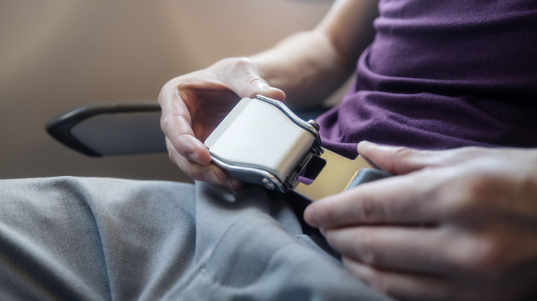 A plane passenger fastening their seatbelt