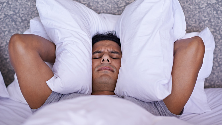 Man with pillow over his ears because of noise in the next cabin