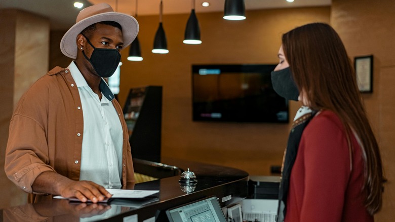 A man wearing a hat speaking to a hotel desk employee