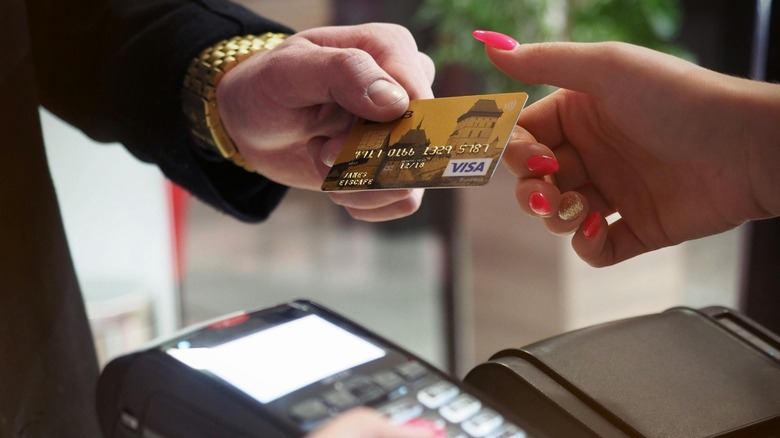 A hand passing a gold credit card to another hand