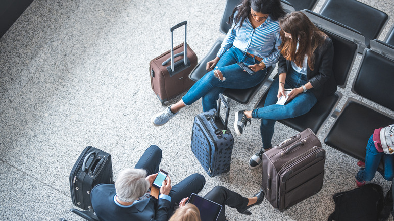 People waiting for their flight at the airport using tablets and phones