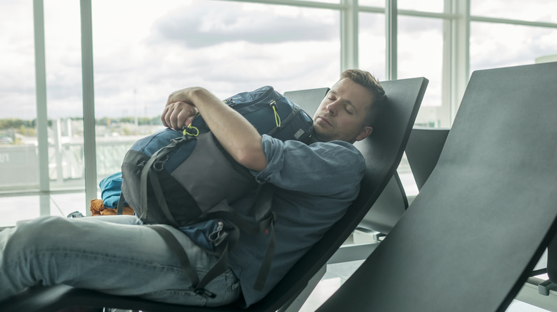 airport man sleeps hugging backpack