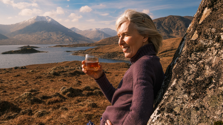 A woman raising a glass of whisky in Scotland.