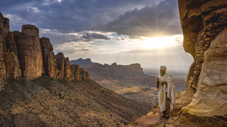 A man standing in the Ethiopian mountains with the sun shining through the clouds