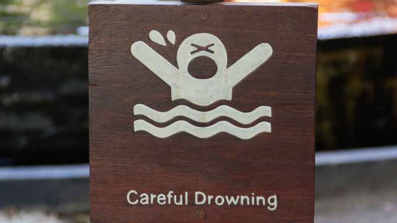 Wooden sign with the words "Careful Drowning" and an image of a swimmer in peril.