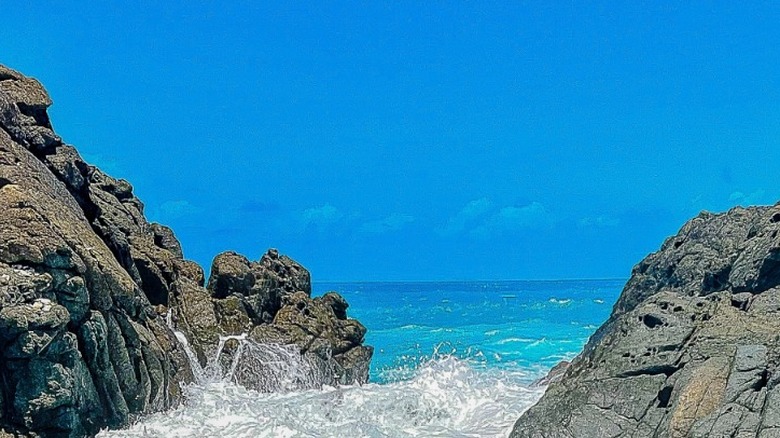 Foamy waves rushing into the Bubbly Pool, from a deep blue sea under a clear blue sky.