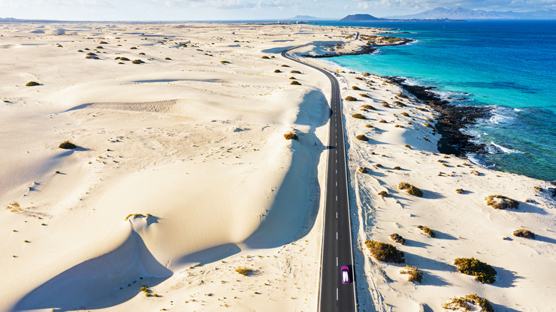 Lone care on highway cutting through sandy dunes by turquise coast line