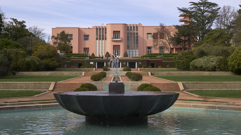 A pink French art deco mansion with a long lawn filled with fountains