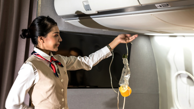 A flight attendant shows where oxygen masks will deploy