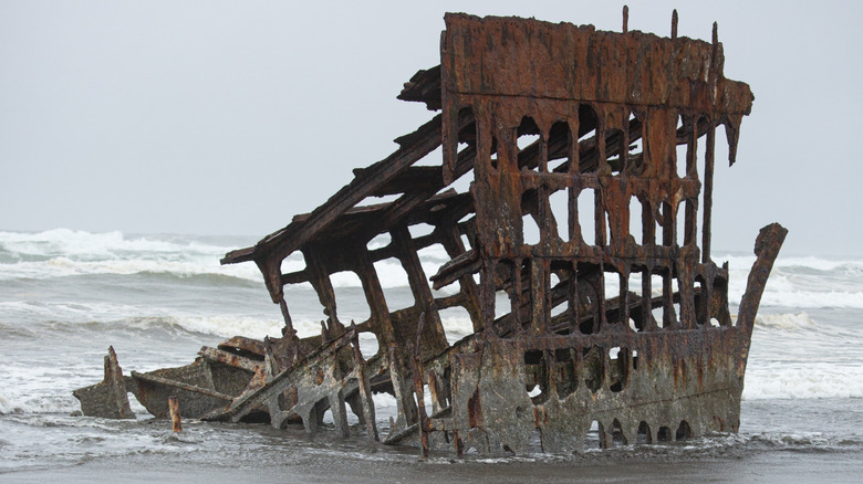 A shipwreck with nothing more than a metal frame on the ocean during a cloudy day