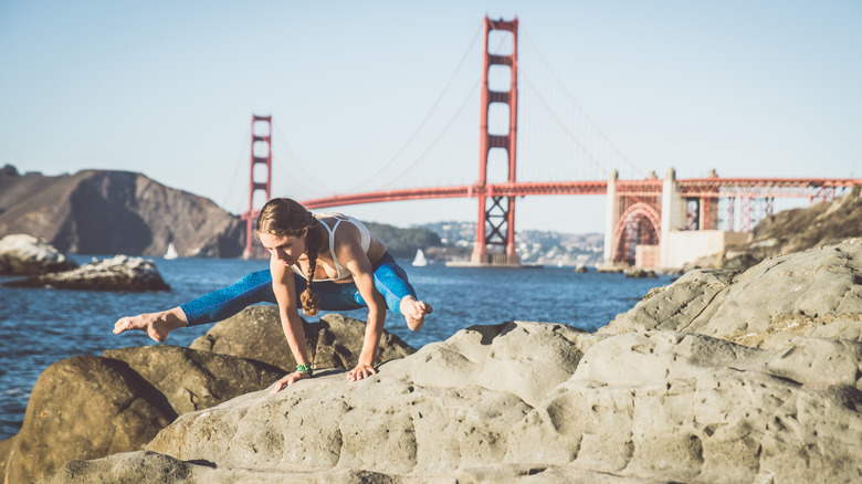 A woman doing a yoga pose on a rock with the Golden Gate Bridge in the background