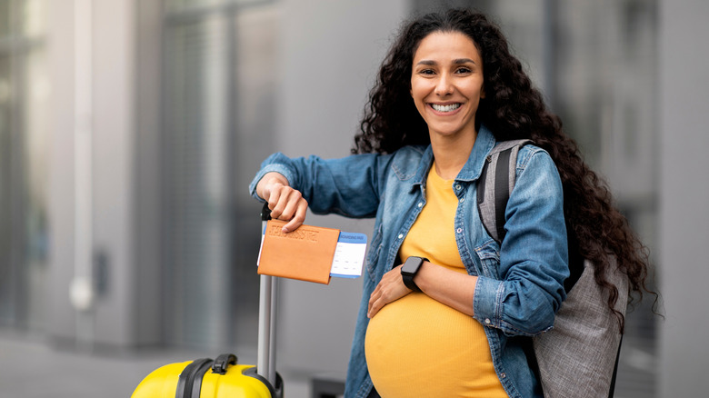 A pregnant traveler with suitcase and passport