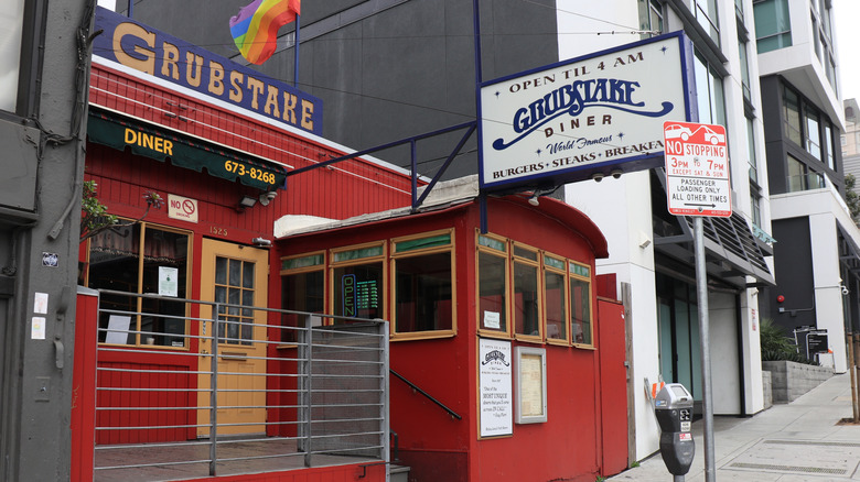 The front of the Grubstake Diner, with a sign, the bright red cable car, and a pride flag waving above