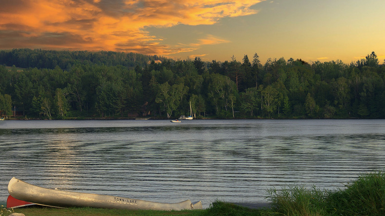 Sunset over a forested lake with a beached canoe in the foreground