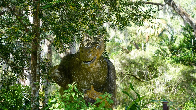 Cement dinosaur statue peering from the brush of the gardens