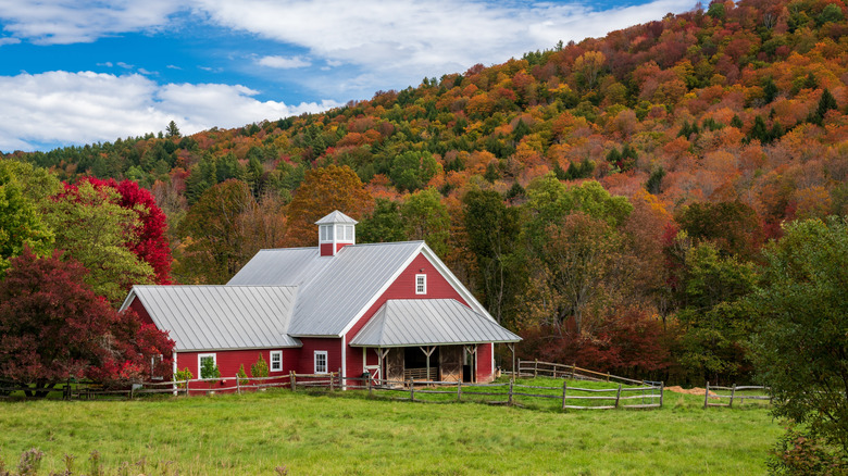 A red barn against a hill of autumn trees