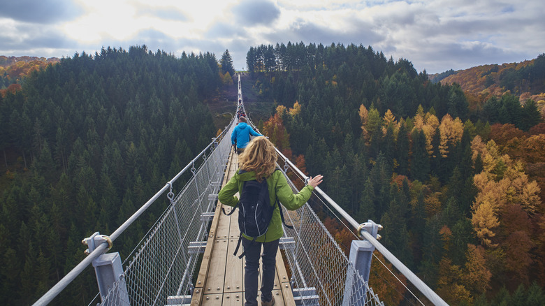 Two people walk across a bridge against fall foliage