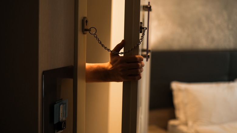 A person entering a hotel door that has a chain on.