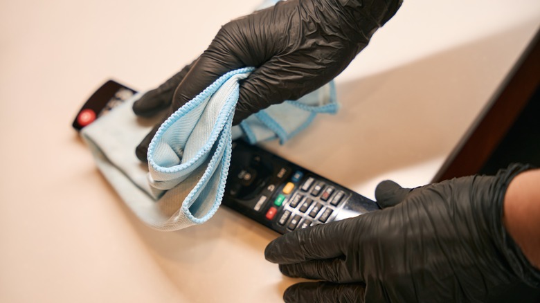 A cleaner in black gloves cleaning a TV remote.