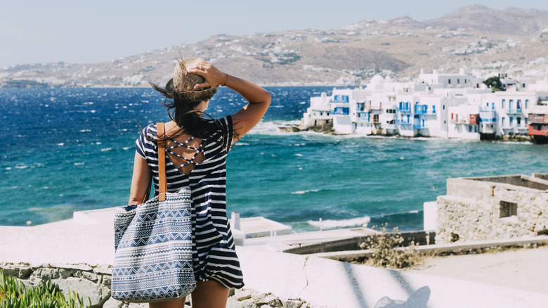 Woman holding her hat as the wind blows across blue water in a bay in Greece