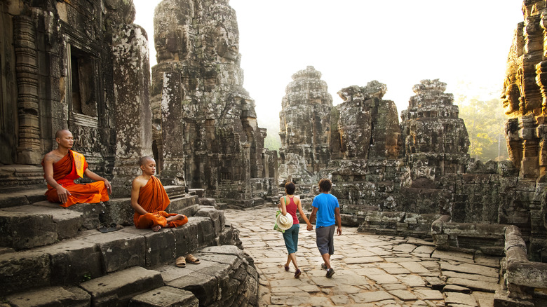 Monks sitting in Cambodian temple as couple walks by