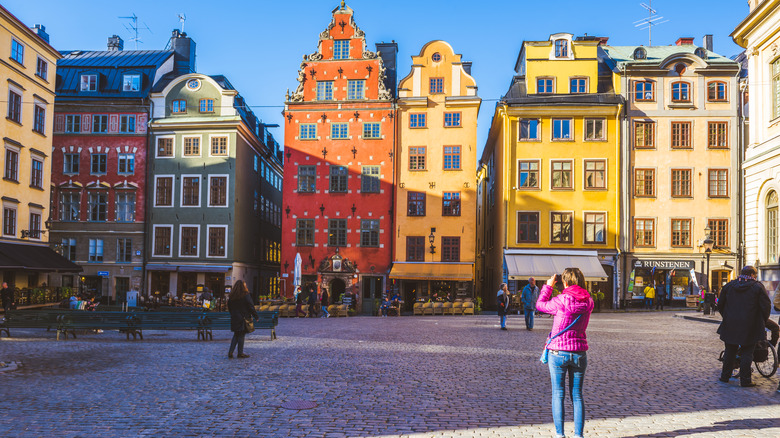 Woman in pink jacket photographing colorful buildings in Sweden