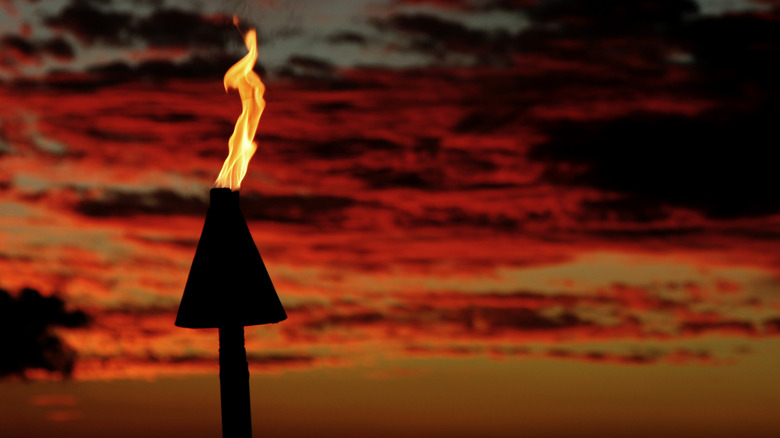 A torch burning at dusk against a red Hawaiian sky