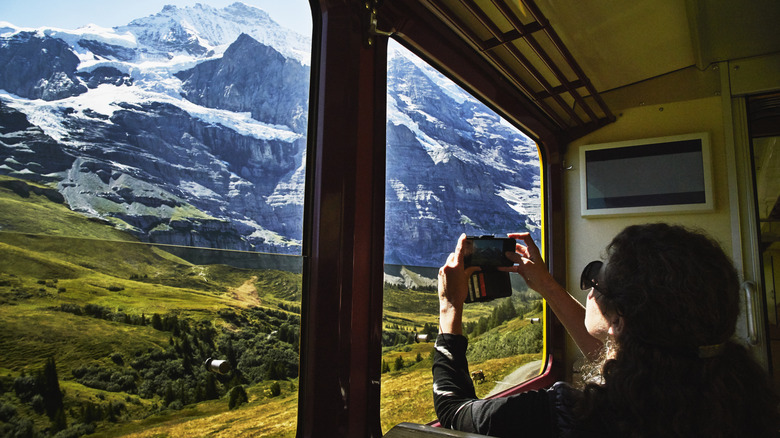 A woman taking a picture of a mountain from a train car