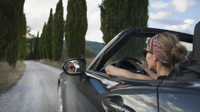 Woman driving past cypress trees, Italy