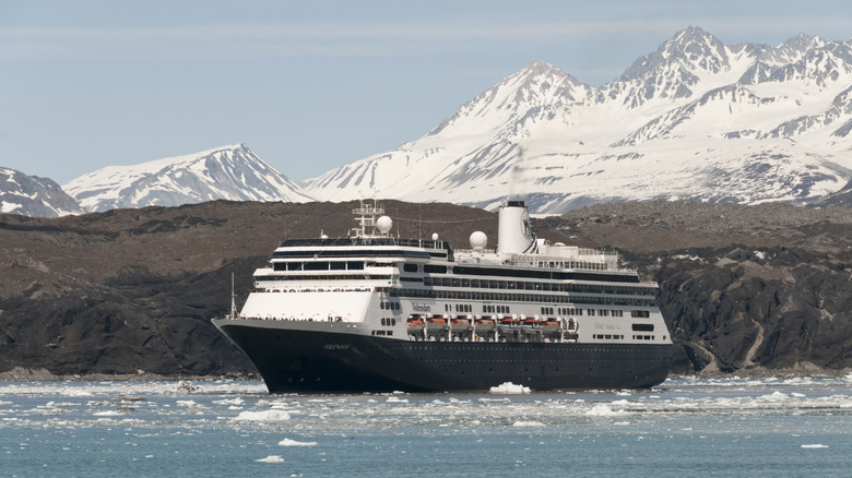 Large cruise ship sets sail against a snow-capped mountain backdrop in Glacier Bay, Alaska