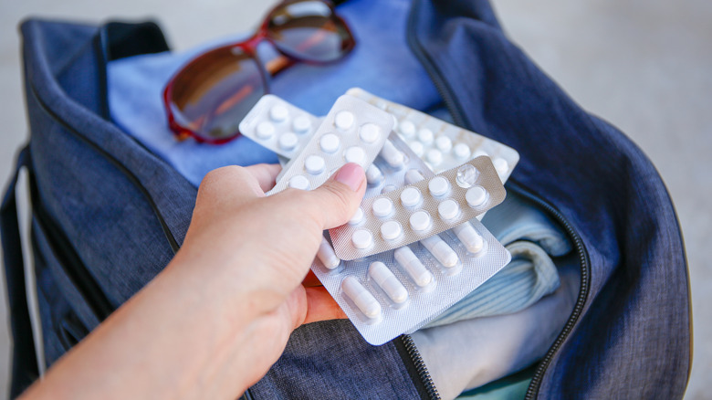 hand holds unlabeled medicine over travel bag