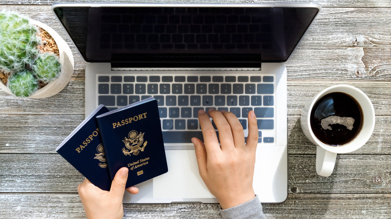 A person using their computer holding two U.S. Passports