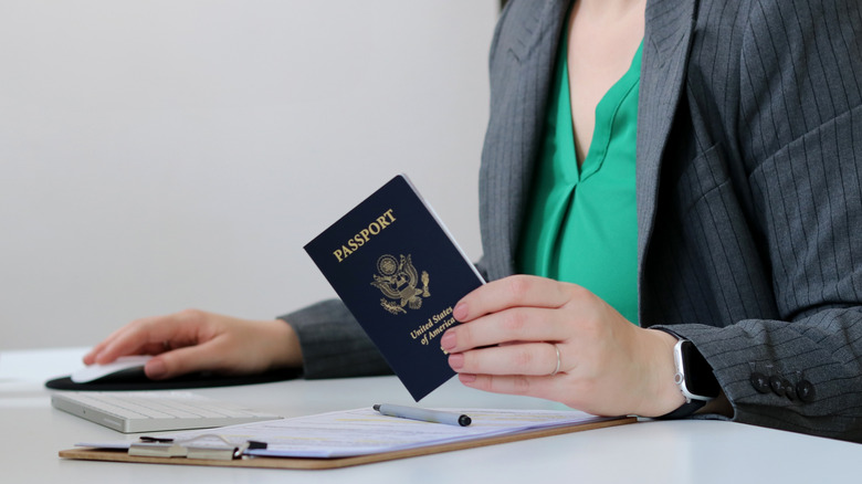 Woman at desk holding passport with papers on a clipboard