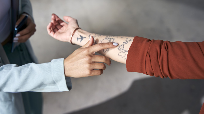 Person touching arm with travel-inspired tattoos