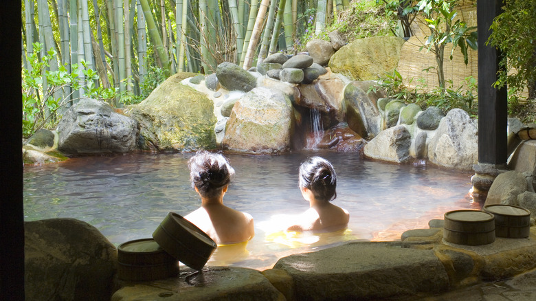 Two women bathing in an outdoor onsen surrounded by bamboo