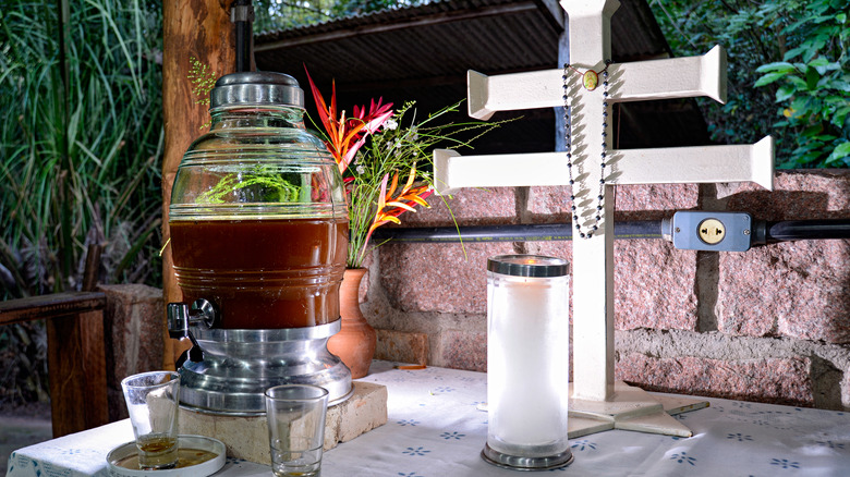 Urn of ayahuasca tea on an altar with a double cross and candle