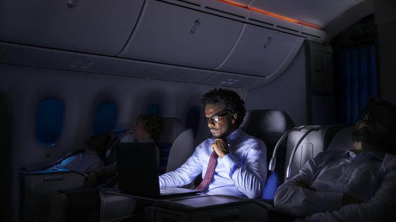 Man using laptop in a dark plane cabin during a red-eye flight