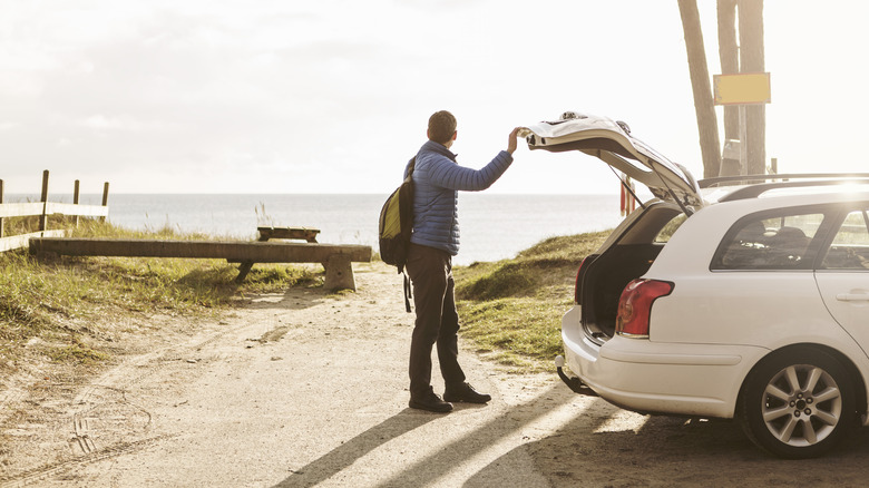 Man closing car trunk and looking over at the beach