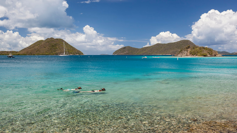 Two snorkelers in shallow water with hilly islands in distance