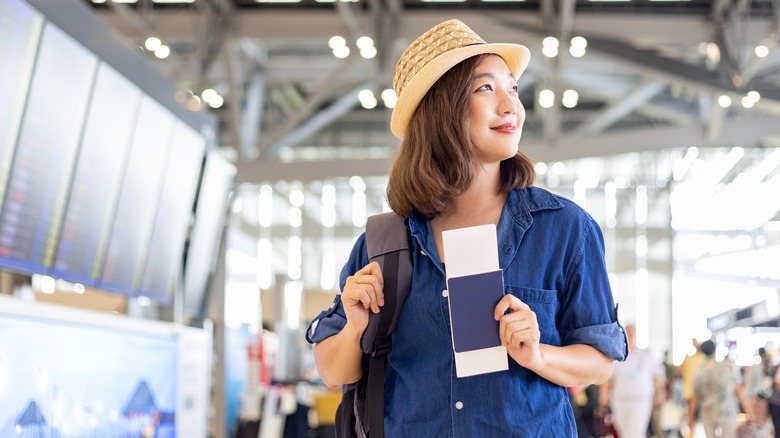 Happy woman in airport holding her boarding pass and passport