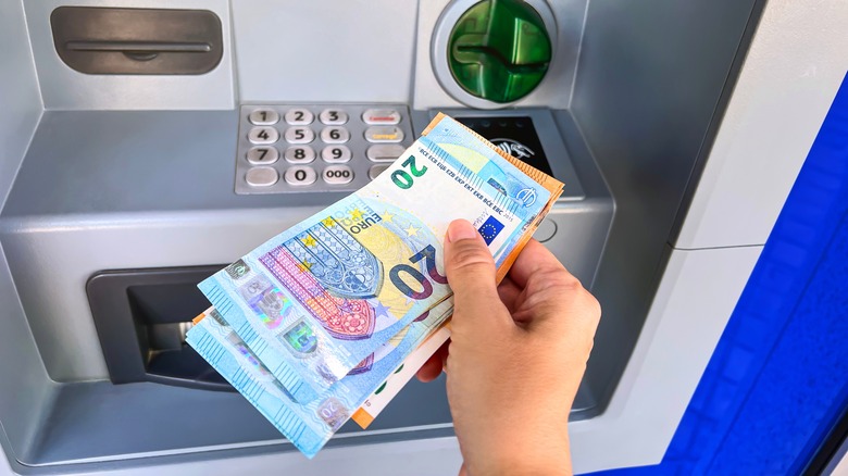 Closeup of hands withdrawing Euro bills from an ATM