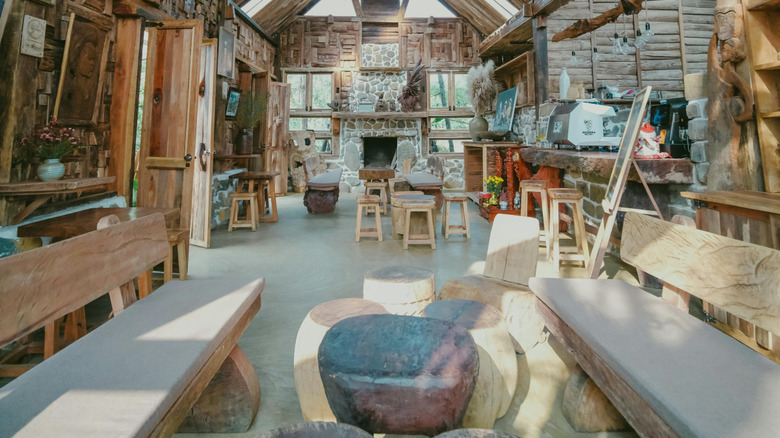 The interior of a wooden lodge with a stone chimney, benches, and more