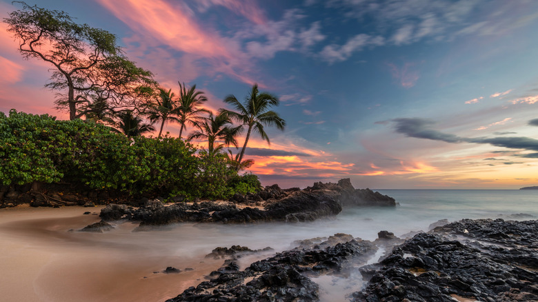 Sunrise at Secret Cove in Maui, Hawaii, with lava rock and palm trees